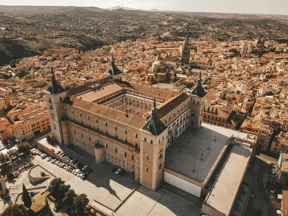 Vista aérea de una gran fortaleza histórica rodeada de una ciudad con edificios antiguos y montañas al fondo.