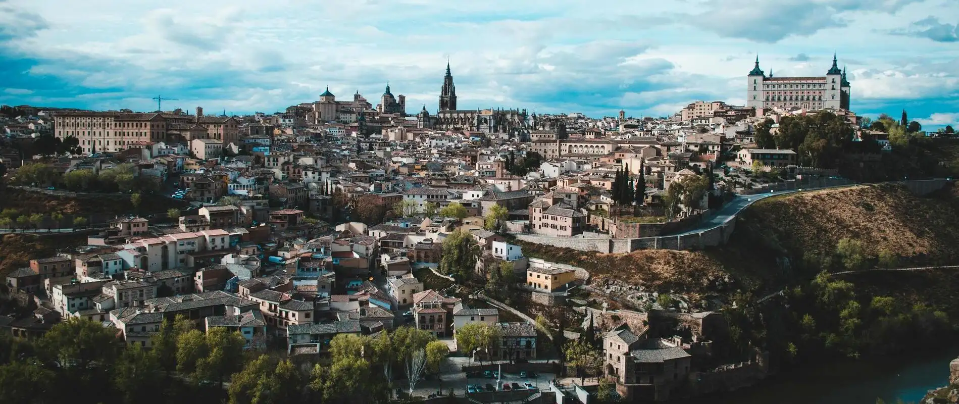 Vista panorámica de una ciudad con edificios históricos y vegetación, bajo un cielo parcialmente nublado.