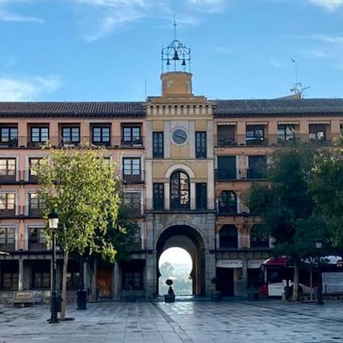 Edificio histórico con un arco central, rodeado de árboles y un cielo azul claro.