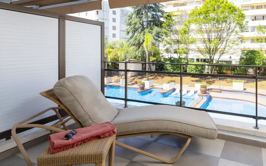 En la terraza con una tumbona, con vistas a la piscina con zonas verdes