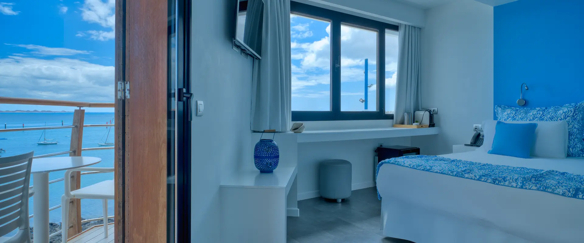 Habitación con cama azul y vista al mar desde el balcón, decorada con tonos azules y blancos.