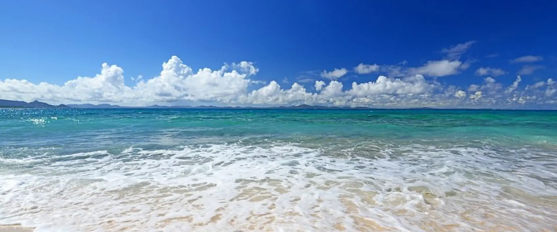 Playa con arena blanca, olas suaves y mar azul turquesa bajo un cielo despejado con nubes esponjosas.