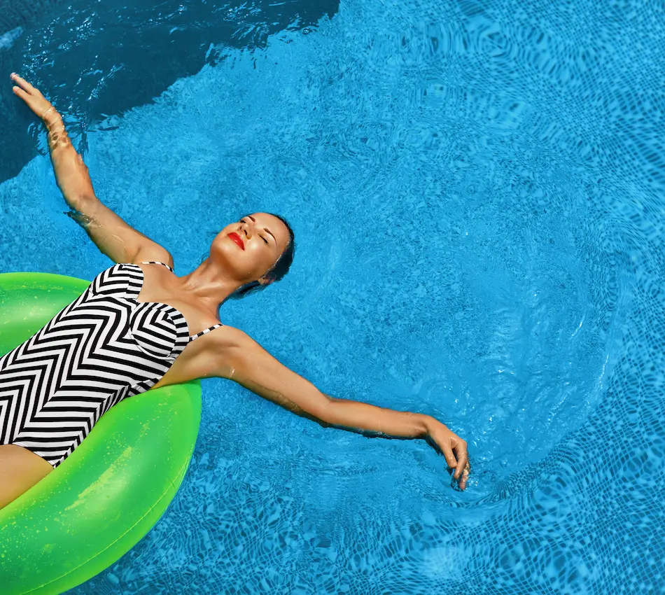 Mujer en traje de baño de rayas flota sobre un inflable verde en una piscina azul, disfrutando del sol.