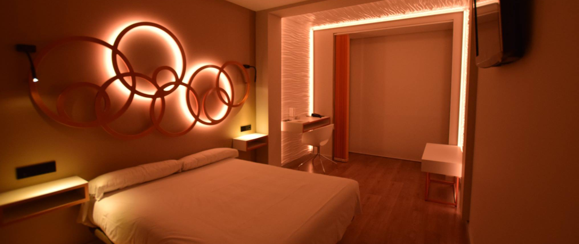 Habitación moderna iluminada en tonos cálidos, con decoración de círculos en la pared y cama blanca.