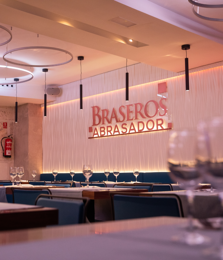 Un elegante restaurante con decoración moderna, mostrando mesas preparadas y un letrero que dice "Braseros Abrasador".
