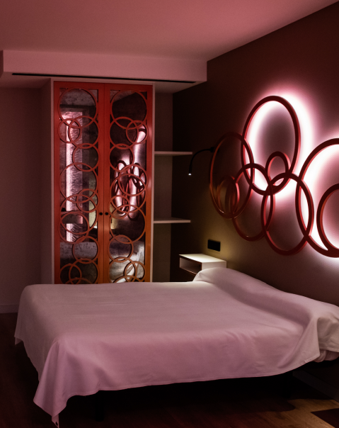 Habitación moderna con cama doble, adornos circulares iluminados en la pared y armario decorado con aros entrelazados.