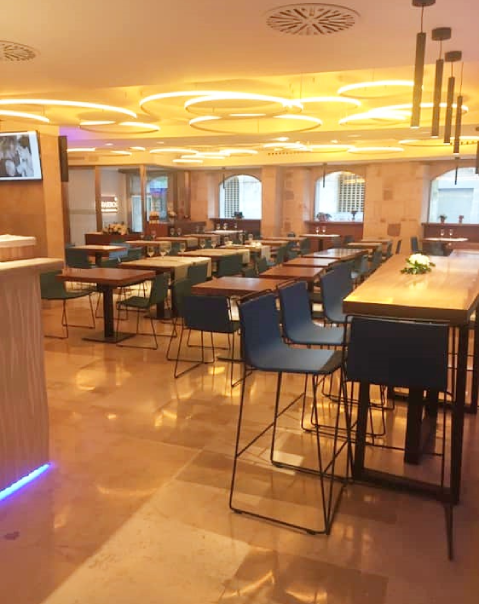 Restaurante moderno y elegante con mesas de madera, sillas azules y luces de diseño en el techo.