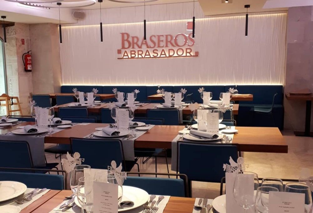 Restaurante elegante con mesas preparadas para servicio, decoración sutil y logo de "Braseros Abrasador" en la pared.