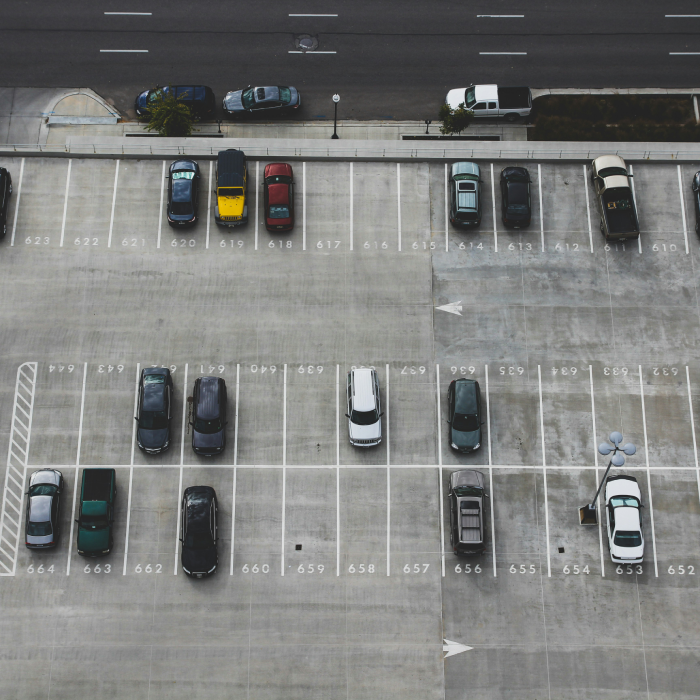 Estacionamiento vacío con pocos autos estacionados, visto desde arriba.