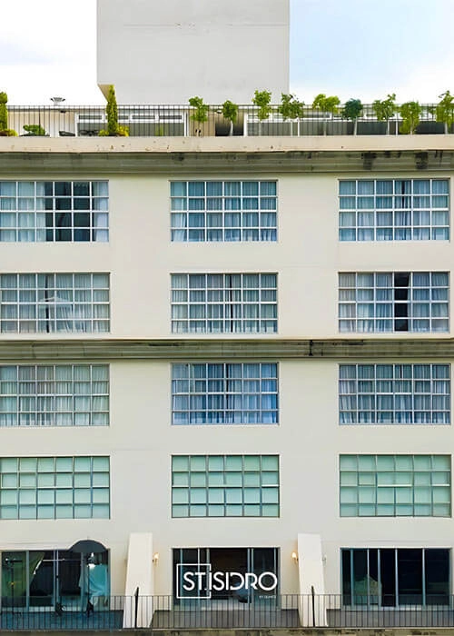 Edificio moderno de varios pisos con ventanas grandes y un letrero que dice "ST. ISIDRO" en la planta baja.