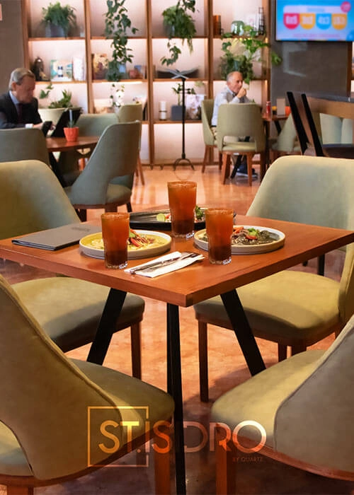 Mesa en restaurante con cuatro platos y vasos de bebida. Varias personas sentadas al fondo en un ambiente acogedor.