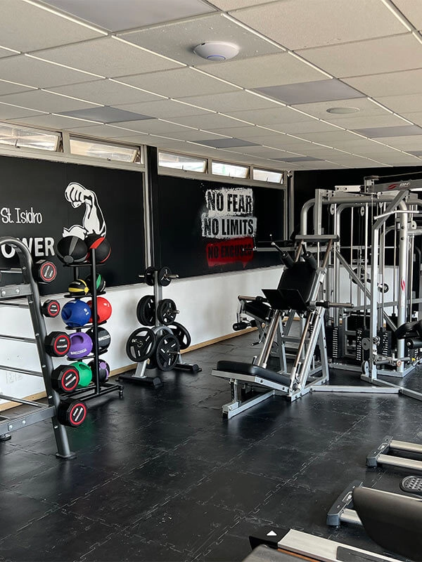 Gimnasio con equipo de pesas y máquinas. En la pared hay un póster que dice "No fear, no limits, no excuses".