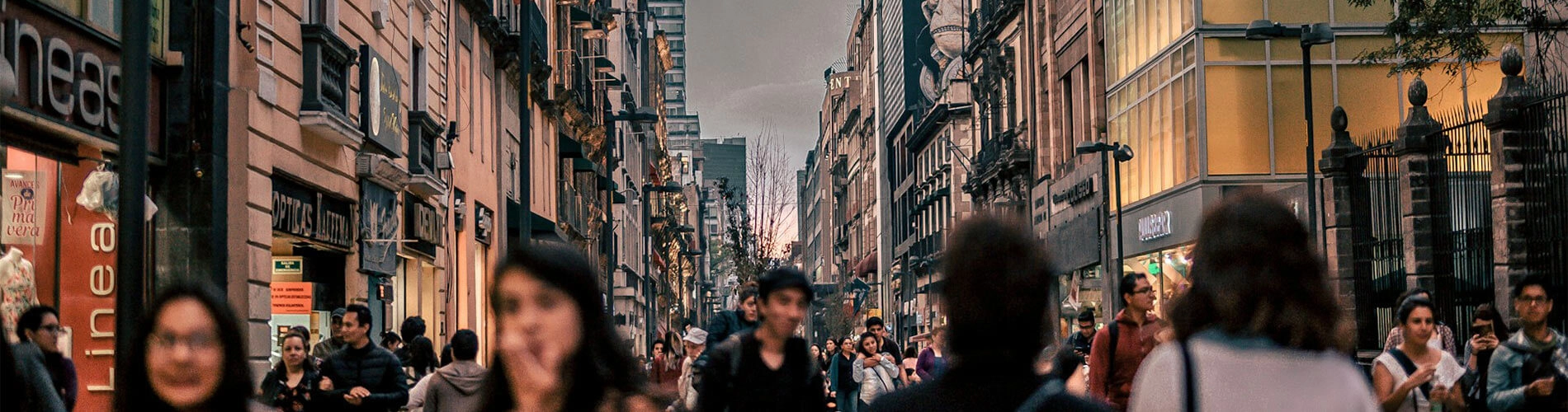 Calle concurrida con personas caminando entre edificios antiguos y modernos al atardecer.