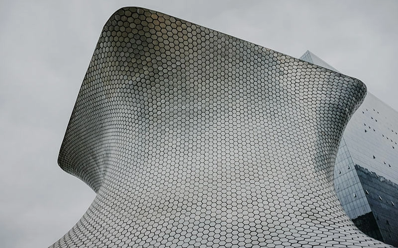 Edificio moderno con diseño curvo y paneles hexagonales, contrastando con el cielo gris al fondo.