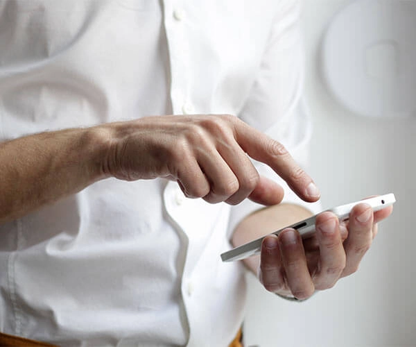 Persona con camisa blanca usando un teléfono móvil con la mano derecha mientras sostiene el dispositivo con la izquierda.