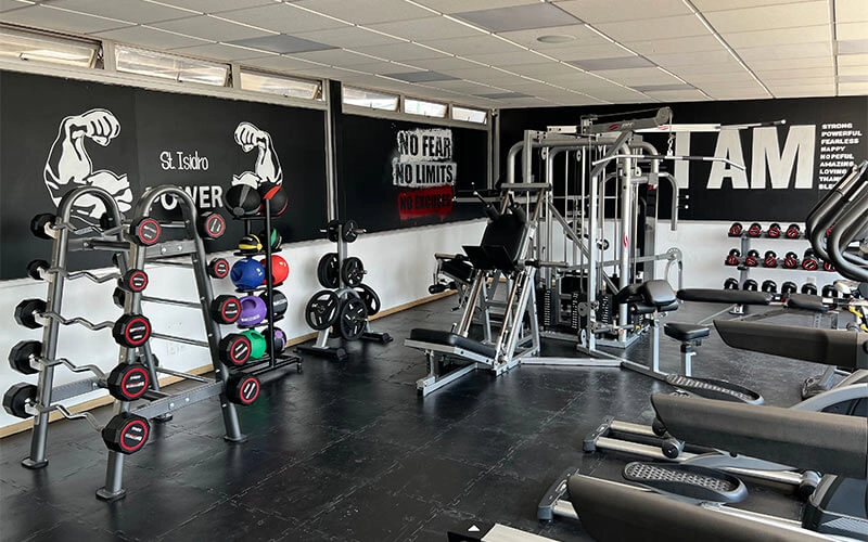 Gimnasio moderno con pesas, equipo de entrenamiento y frases motivacionales en las paredes.