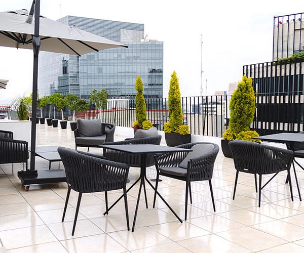 Terraza moderna con mesas y sillas negras, plantas decorativas y edificio de cristal al fondo.