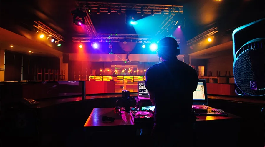DJ mezclando música en una discoteca iluminada con luces de colores.