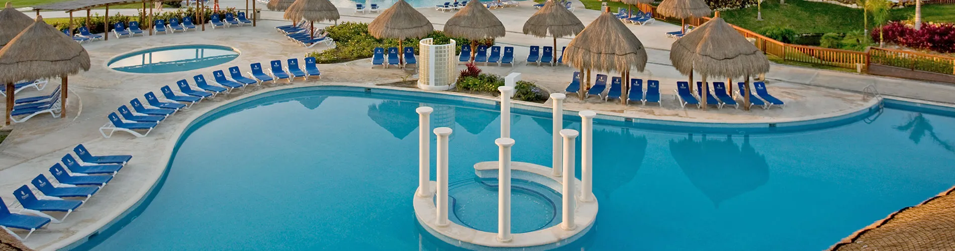 Piscina grande con tumbonas azules y sombrillas de palma alrededor, ideal para descansar y disfrutar del sol.
