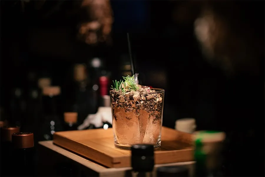Un cóctel en vaso corto con decoraciones de hierbas y piedras sobre una tabla de madera.