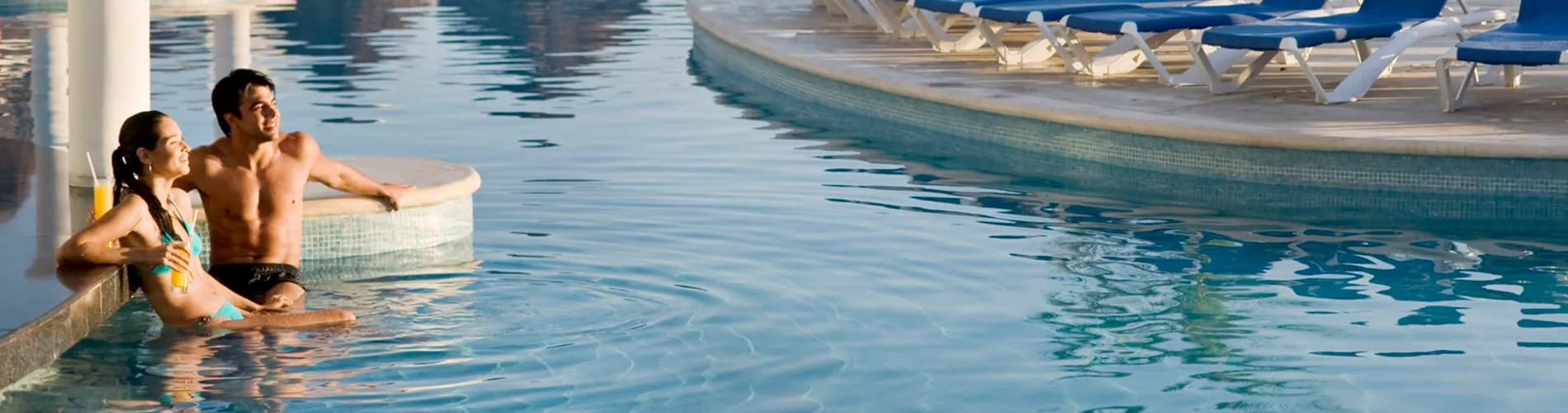Pareja disfrutando de un cóctel en la piscina, con tumbonas alrededor del borde.