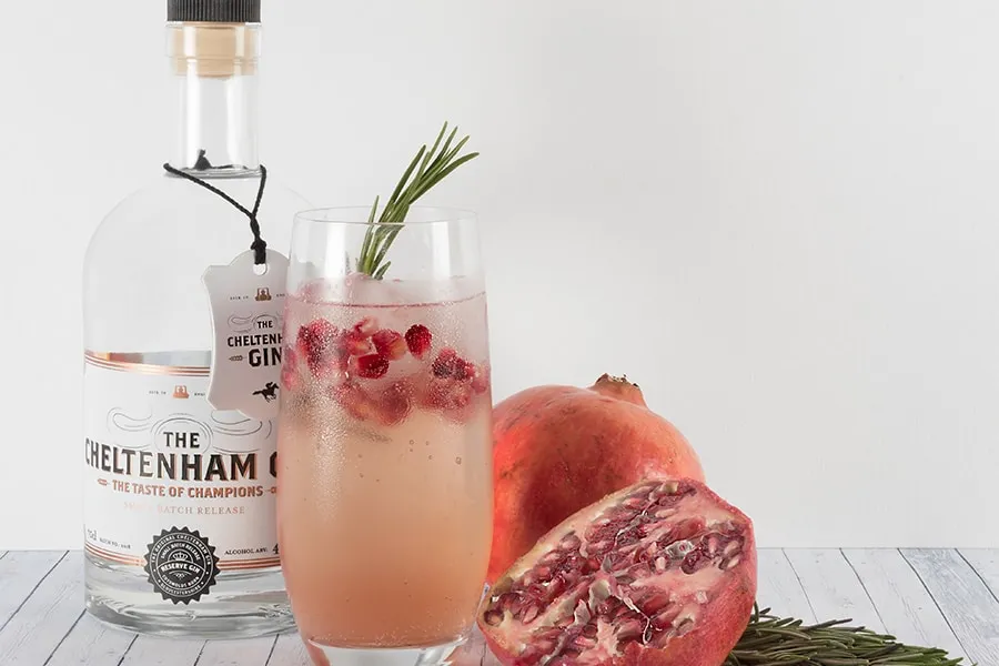 Botella de ginebra, vaso con bebida de granada y ramita de romero. Granadas de fondo.