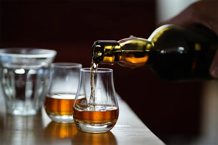 Botella sirviendo licor en vasos pequeños sobre una mesa de madera.