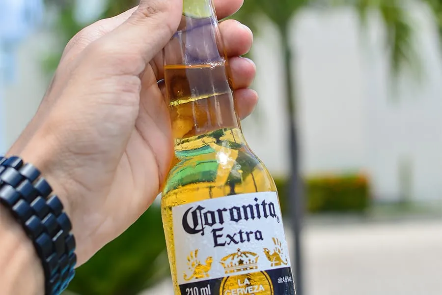 Persona sosteniendo una botella de cerveza Coronita Extra al aire libre.