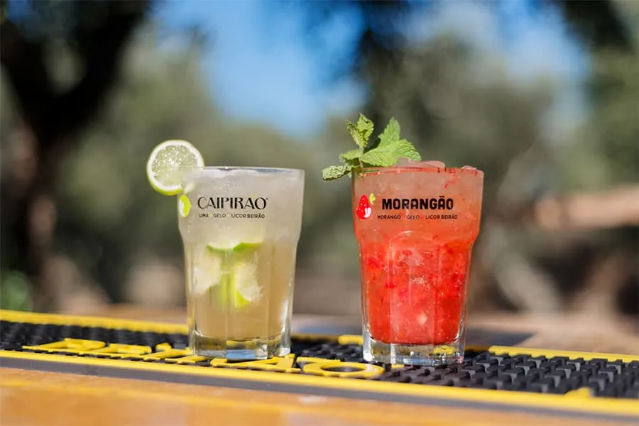 Dos cócteles refrescantes en vasos, uno de lima y otro de fresa, sobre una barra al aire libre.
