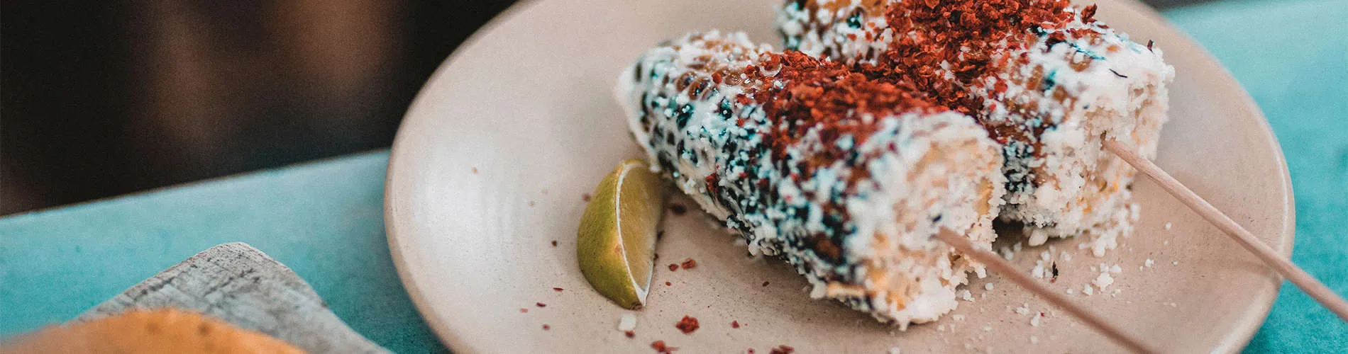 Elotes con mayonesa, queso y chile en un plato, acompañados de un limón.