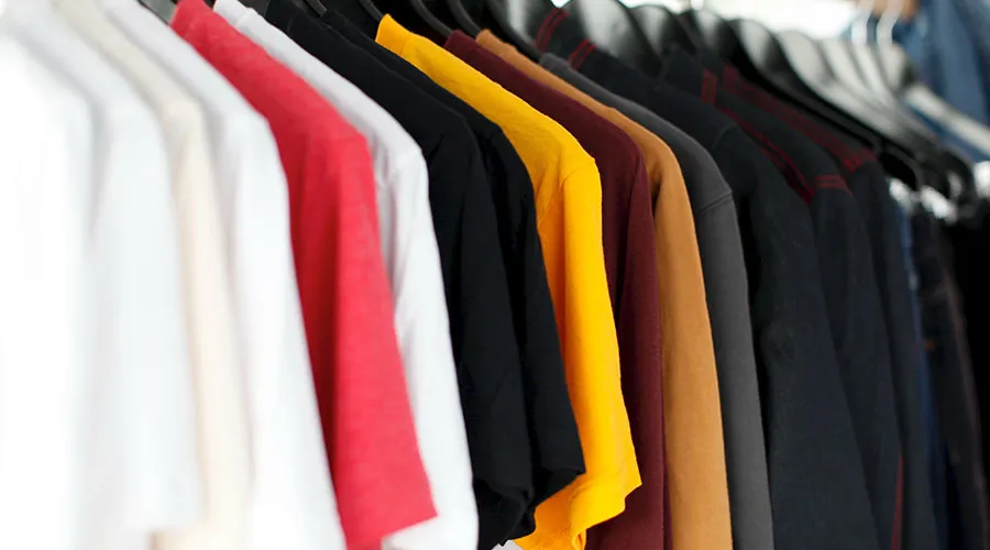 Camisetas de varios colores colgadas en perchas, con tonos como blanco, rojo, negro y amarillo.