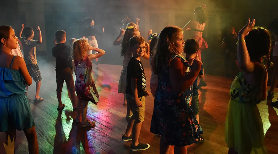 Niños y niñas bailando en una pista de baile iluminada con luces coloridas.