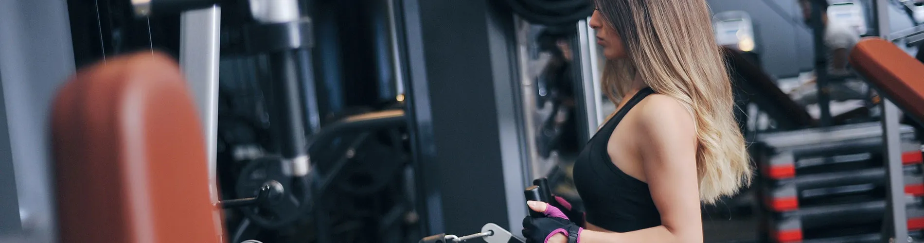 Mujer ejercitándose en el gimnasio, usa guantes y tiene el cabello largo suelto.
