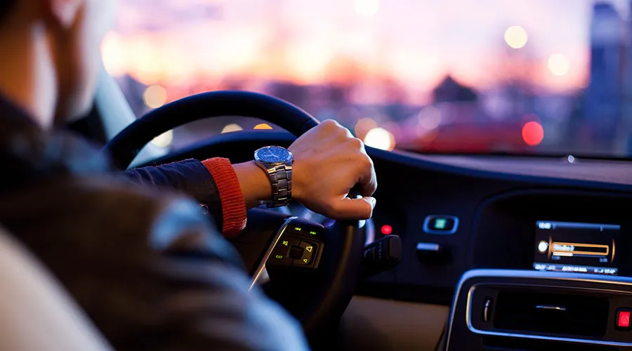 Persona conduciendo un auto al atardecer, con una mano en el volante y un reloj en la muñeca.