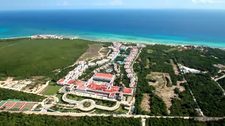 Vista aérea de un complejo turístico junto al mar rodeado de vegetación y canchas deportivas.