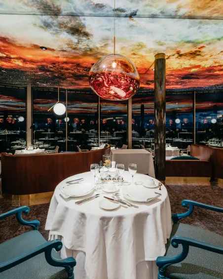 Mesa elegante en restaurante con lámparas esféricas y techo con diseño de cielo al atardecer.