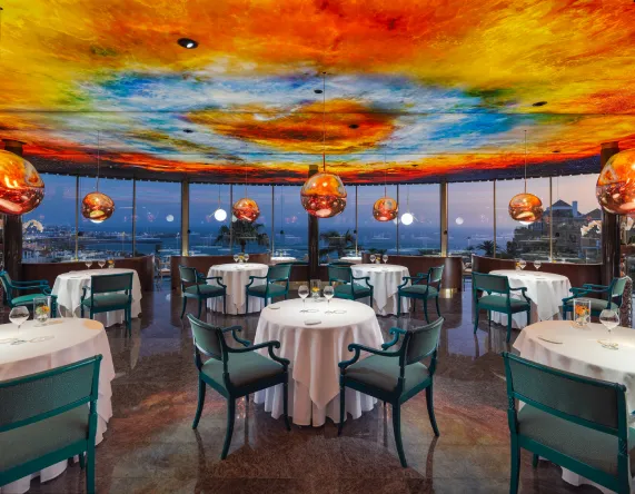 Restaurante elegante con techo colorido, mesas redondas y vista panorámica.
