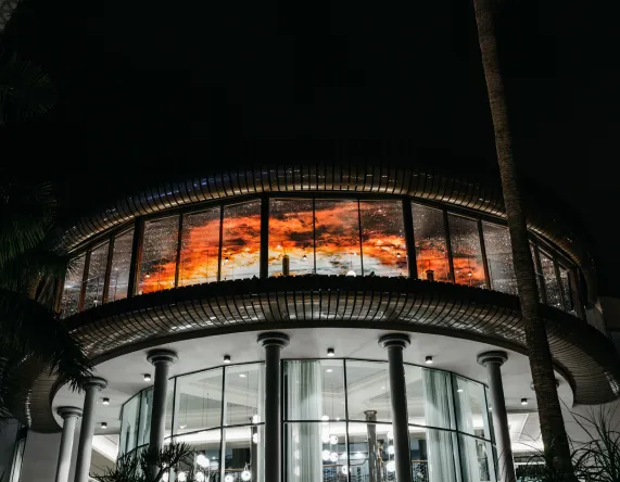 Edificio curvo con ventanales iluminados y cielo rojo reflejado, noche.