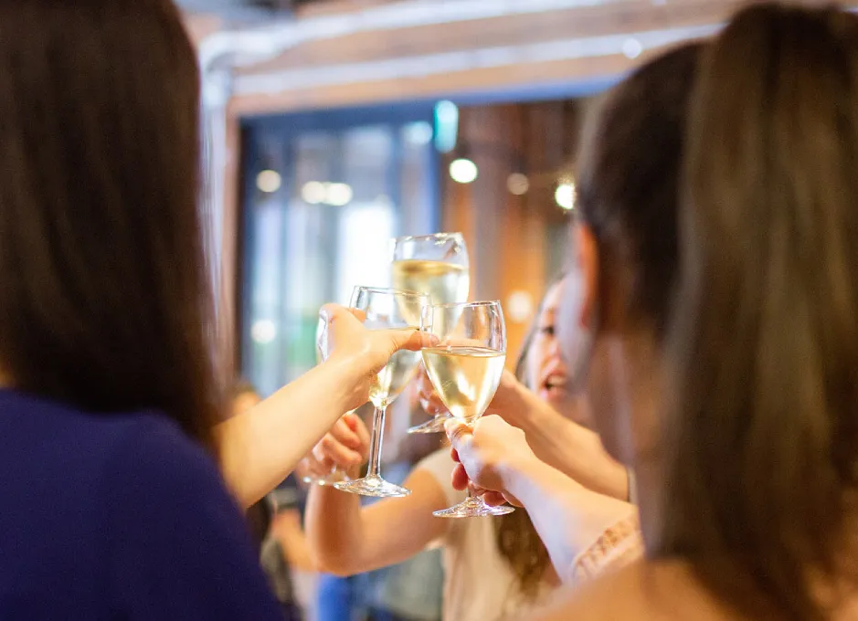 Personas brindando con copas de vino blanco en un ambiente festivo.