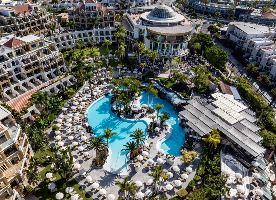 Vista aérea de un complejo hotelero con piscina, sombrillas y jardines.