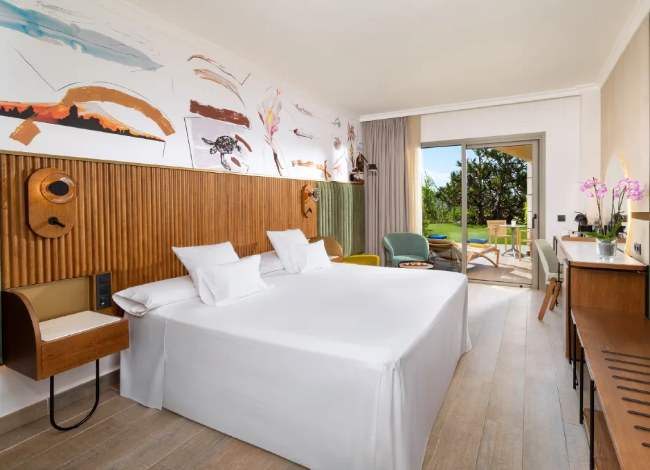 Habitación moderna con cama doble, decoración artística, y balcón con vista al jardín.