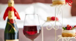 Copa de vino tinto junto a una botella de champán y postres en una bandeja blanca.