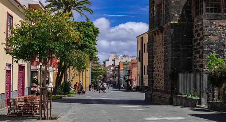 Calle peatonal con árboles y edificios históricos bajo un cielo azul con nubes esponjosas.