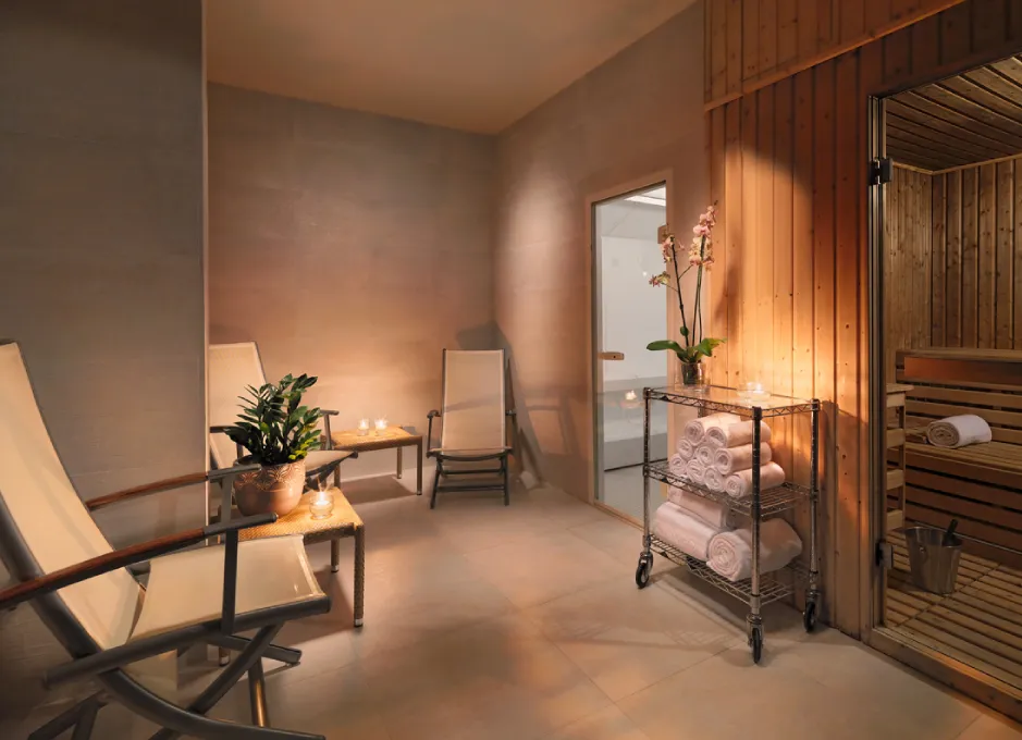 Sala de spa con sillas reclinables, toallas, sauna de madera y orquídea en un carrito.