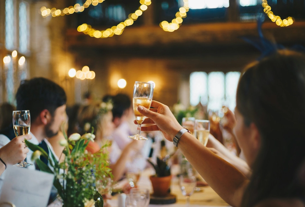 Personas brindando con copas en una celebración, luces cálidas de fondo.