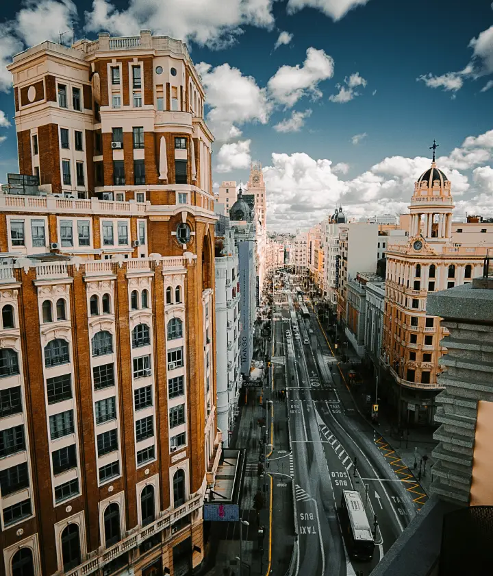 Vista aérea de una calle concurrida en Madrid, con edificios históricos y cielo nublado.