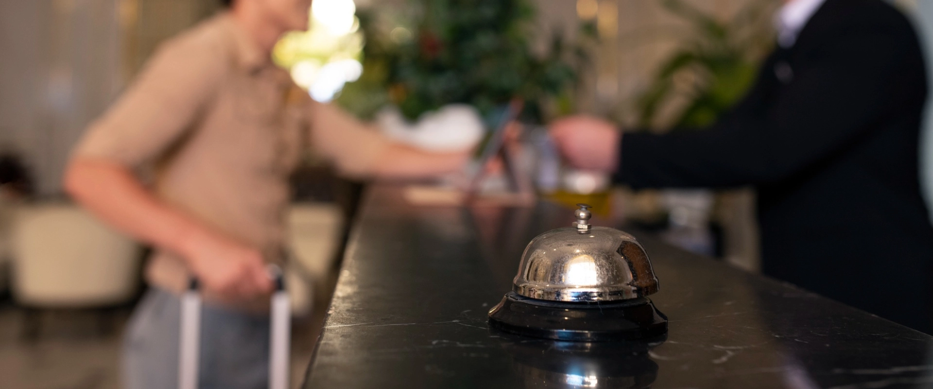 Campana en mostrador de hotel, con personas en segundo plano interactuando en la recepción.