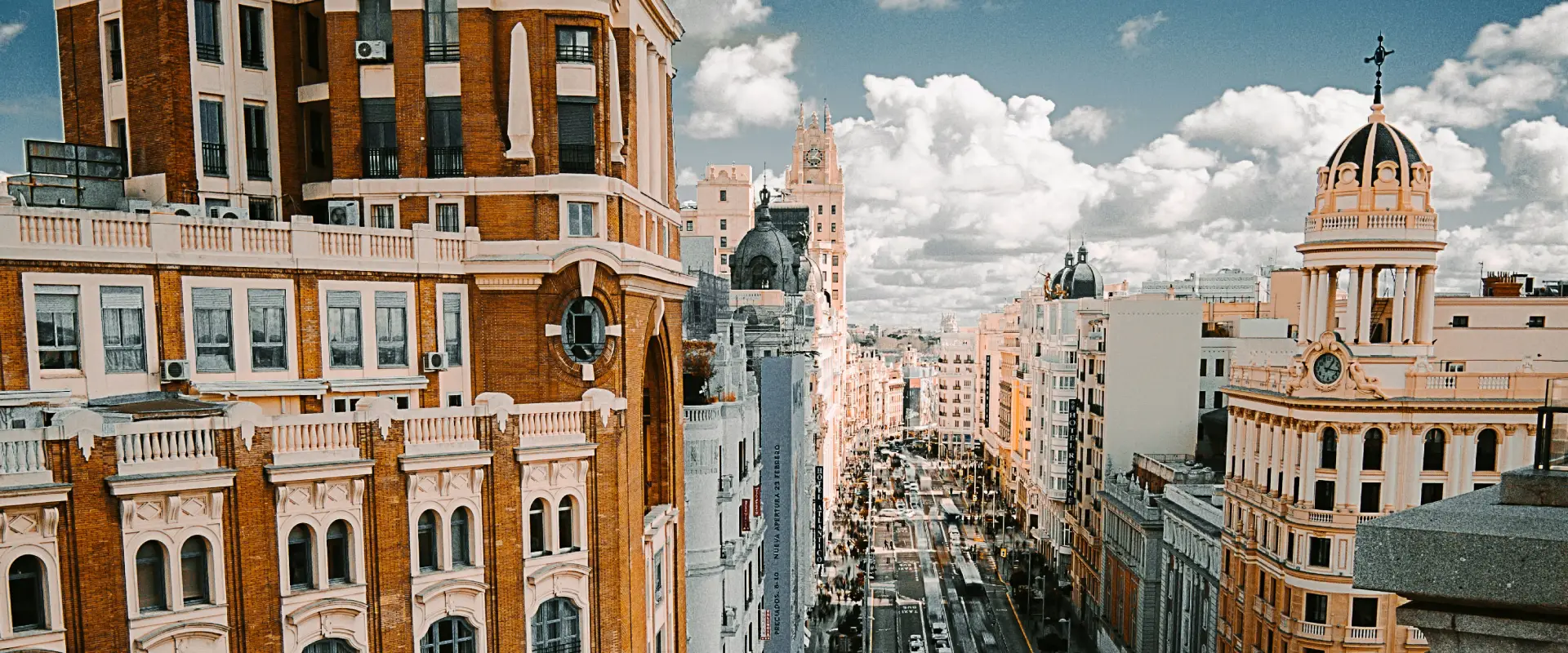 Vista aérea de una calle de Madrid, con edificios históricos de ladrillo rojo y cielo nublado.