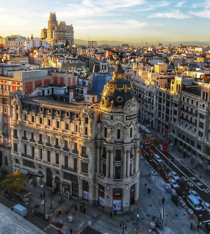 Vista aérea de un edificio histórico iluminado por el sol al atardecer en una concurrida intersección urbana.