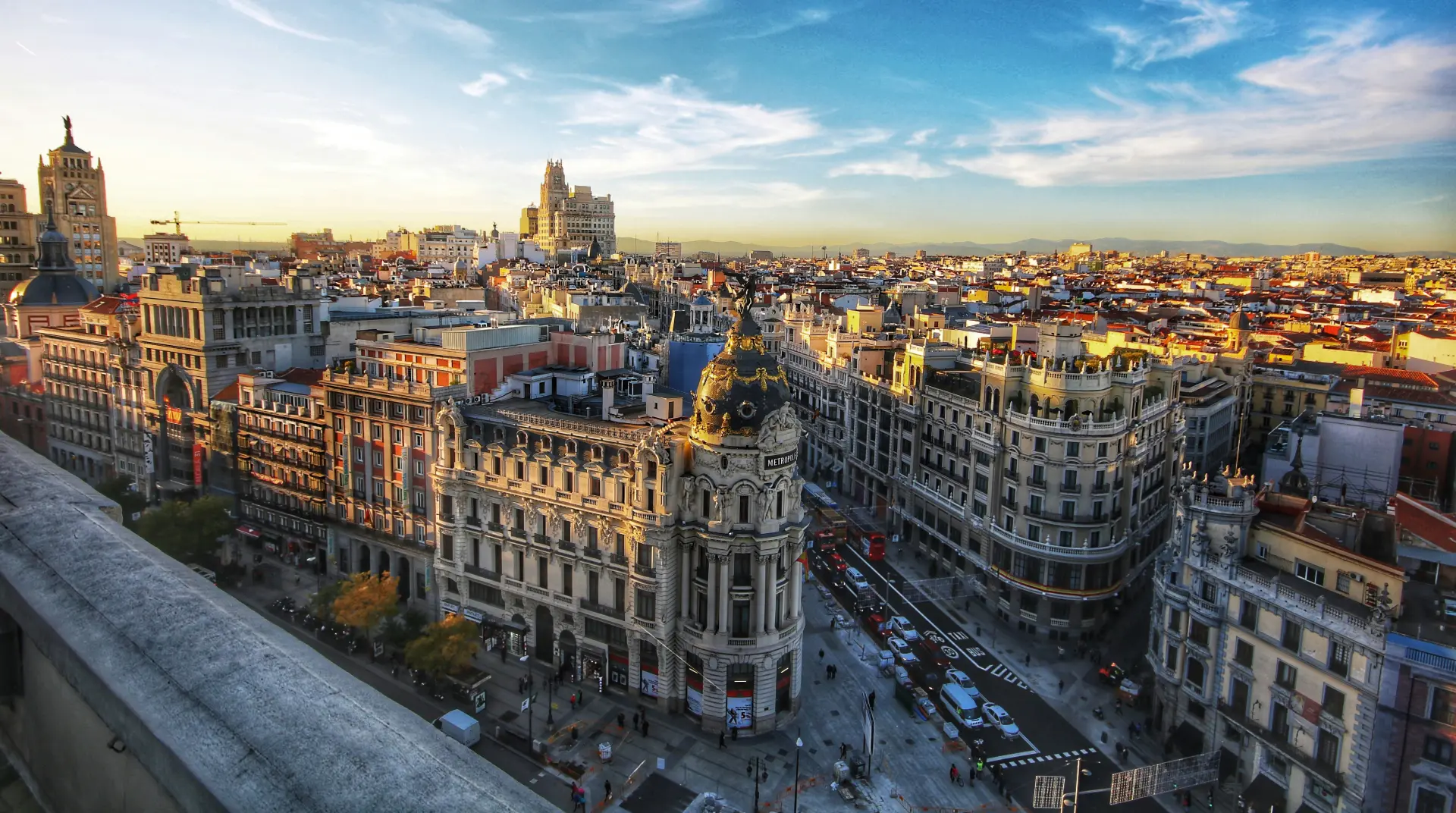 Vista aérea de una ciudad con edificios históricos iluminados por el sol, y un cielo azul con algunas nubes.